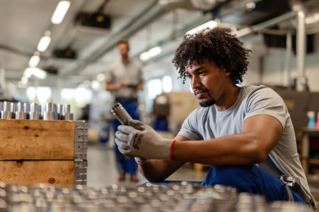 Young worker examining stainless steel cylinder rod while working in warehouse