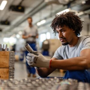 Young worker examining stainless steel cylinder rod while working in warehouse